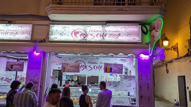 Heladería iluminada de noche con rótulos lilas y clientes eligiendo sabores