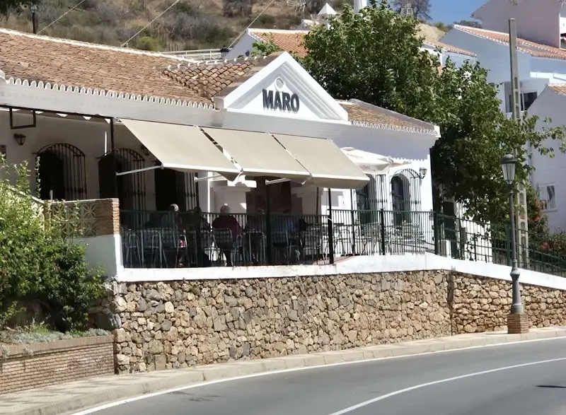 Edificio blanco con rótulo de Maro, terraza con toldos y muro de piedra junto a la carretera