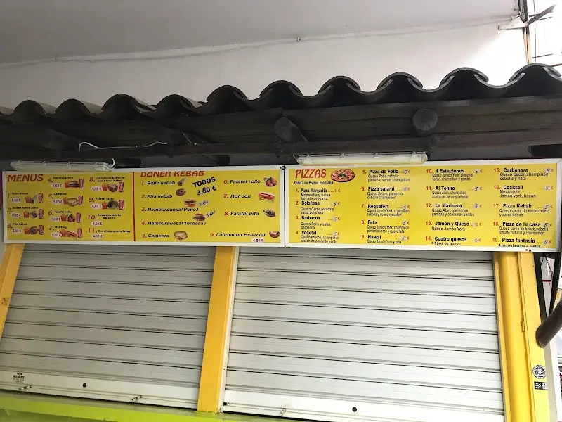 Carteles de menús, döner kebab a 3,60 € y pizzas sobre la persiana cerrada del local