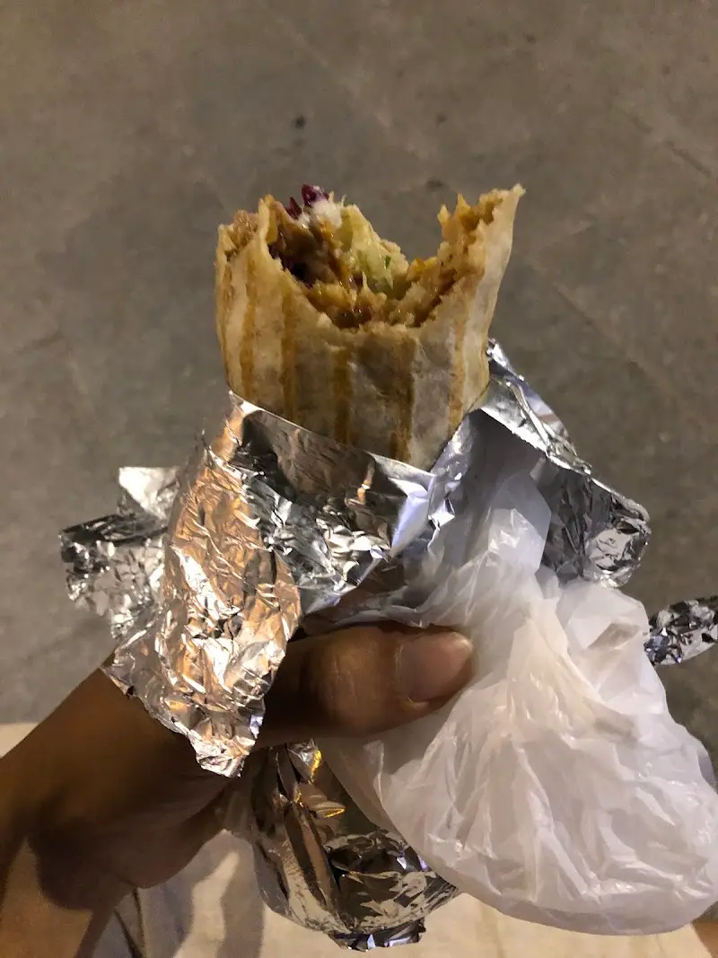 Kebab enrollado a medio comer en la mano, envuelto en aluminio y bolsa
