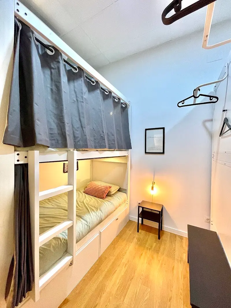 Litera con cortina gris para la cama de arriba, mesilla y lámpara encendida