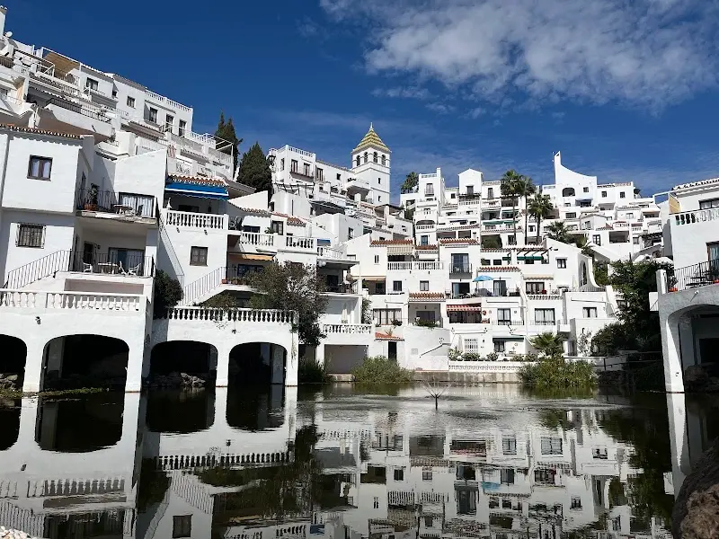 Casas blancas con arcos y una torre reflejadas en el estanque del Ancladero