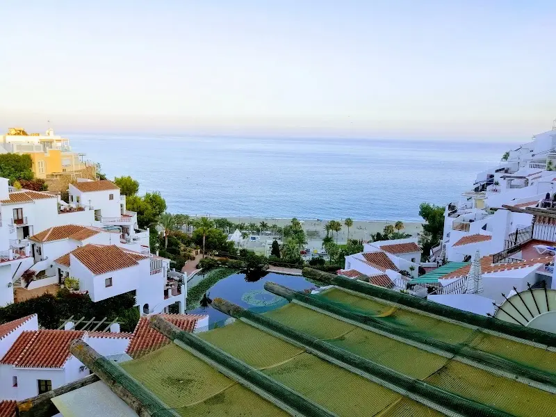 Tejados, estanque y la playa con el mar en calma al amanecer, desde lo alto del complejo