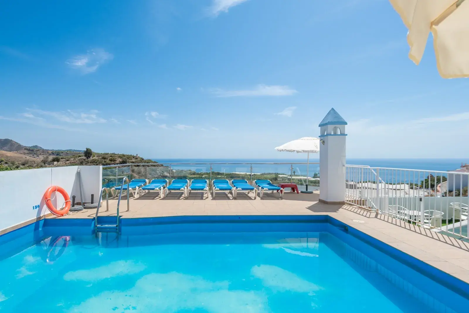Piscina en la azotea del Playamaro con tumbonas azules y el mar al fondo