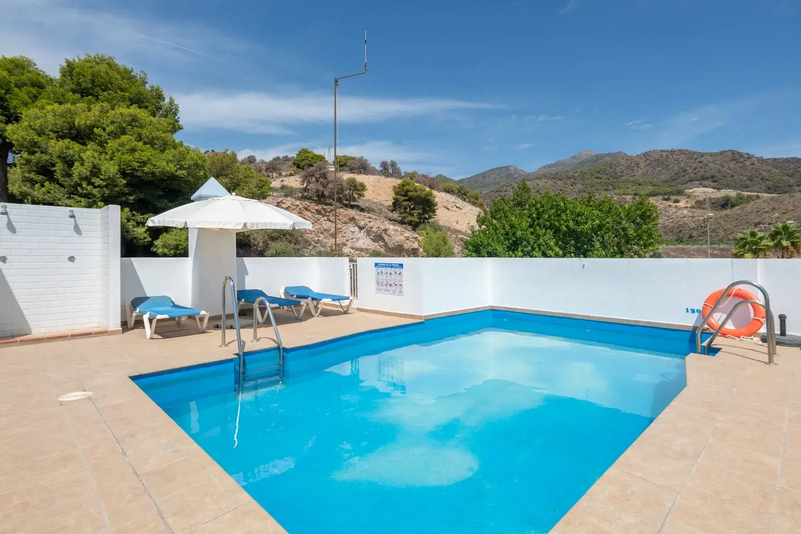 Piscina con sombrillas y tumbonas junto a la ladera arbolada de Maro