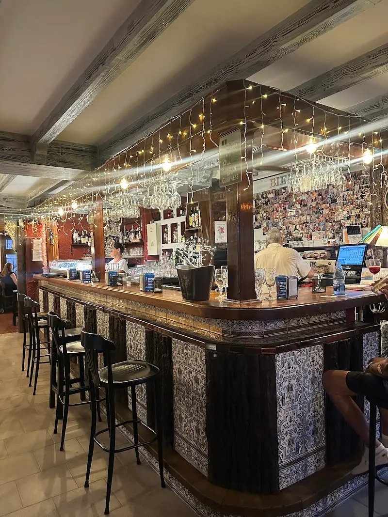 Barra de madera con azulejos, taburetes altos y guirnalda de luces sobre las copas colgadas