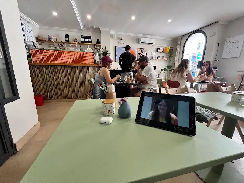 Interior de la cafetería con mesas verde pastel, barra de caña y clientes