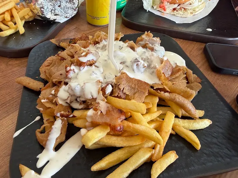 Plato de carne de kebab sobre patatas fritas con salsa blanca en una bandeja negra