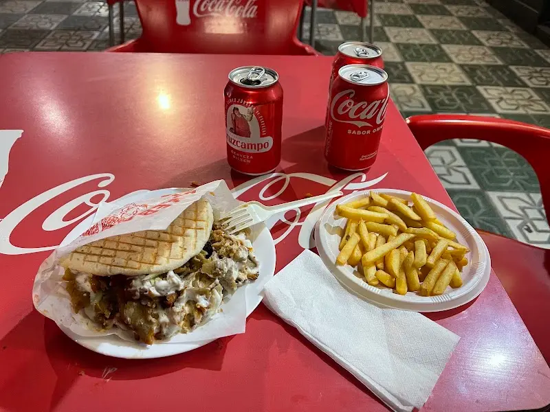 Kebab en pan de pita con salsa blanca y patatas fritas junto a latas de refresco y cerveza