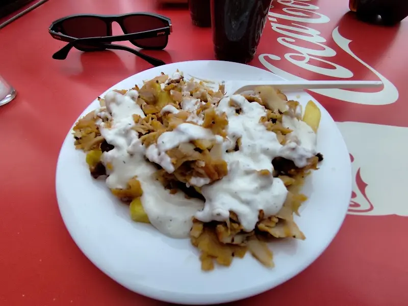 Plato de carne de kebab con patatas y salsa blanca sobre mesa roja