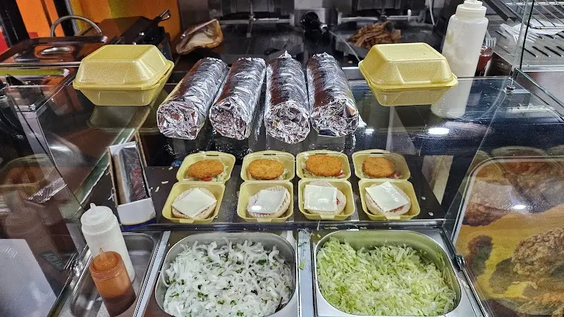 Mostrador con rollos de kebab en papel de aluminio, hamburguesas y bandejas de cebolla y lechuga
