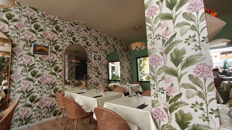 Sala con papel pintado de flores y hojas, espejos en arco y mesas con mantel blanco