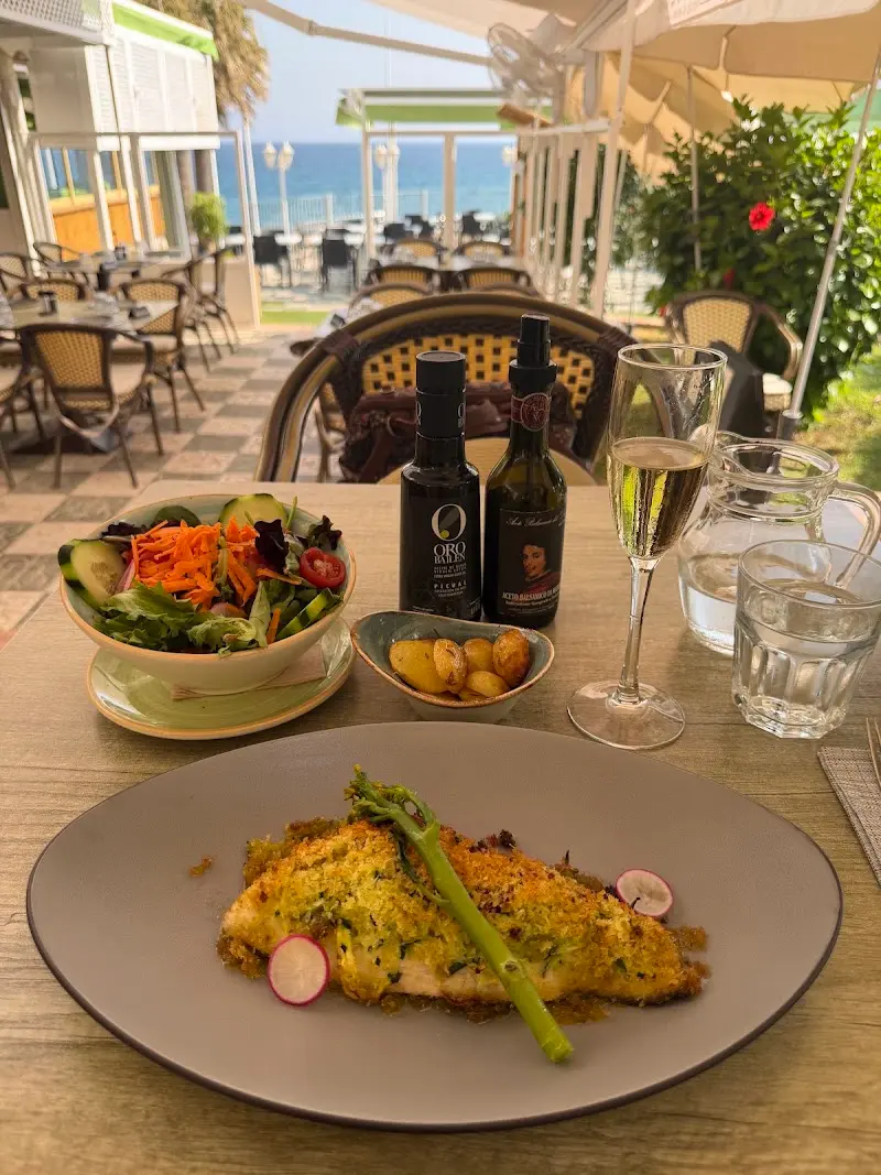 Pescado gratinado con espárrago, ensalada y copa de vino en la terraza frente al mar