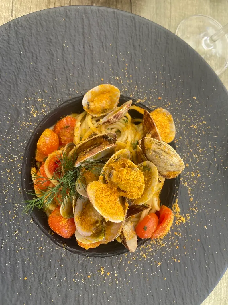 Espaguetis con almejas, tomates cherry y pan rallado tostado en plato negro