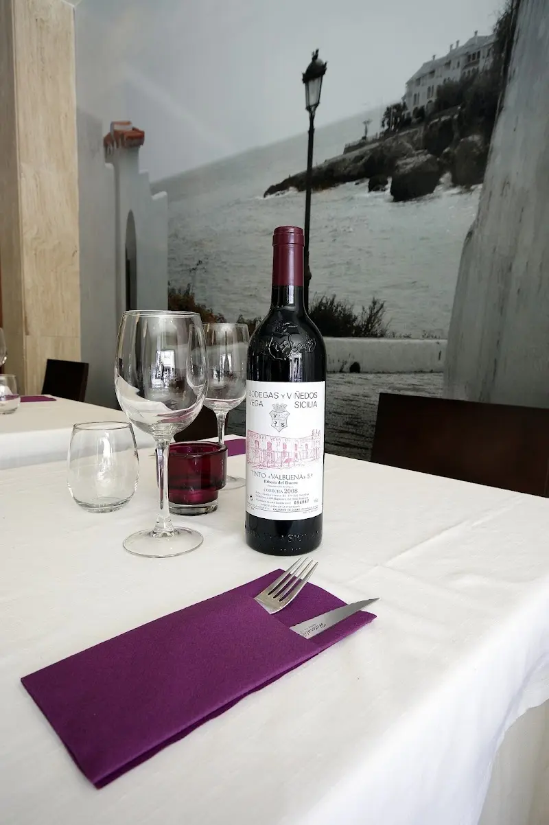 Mesa con mantel blanco, copas y botella de Valbuena 5º ante un mural de la costa de Nerja