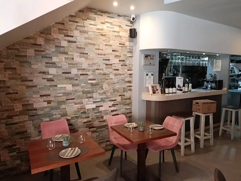 Comedor con pared de piedra, sillas rosas tapizadas y barra con copas colgadas