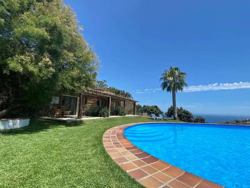 Piscina junto al césped y la casa de piedra con porche, y el mar en el horizonte