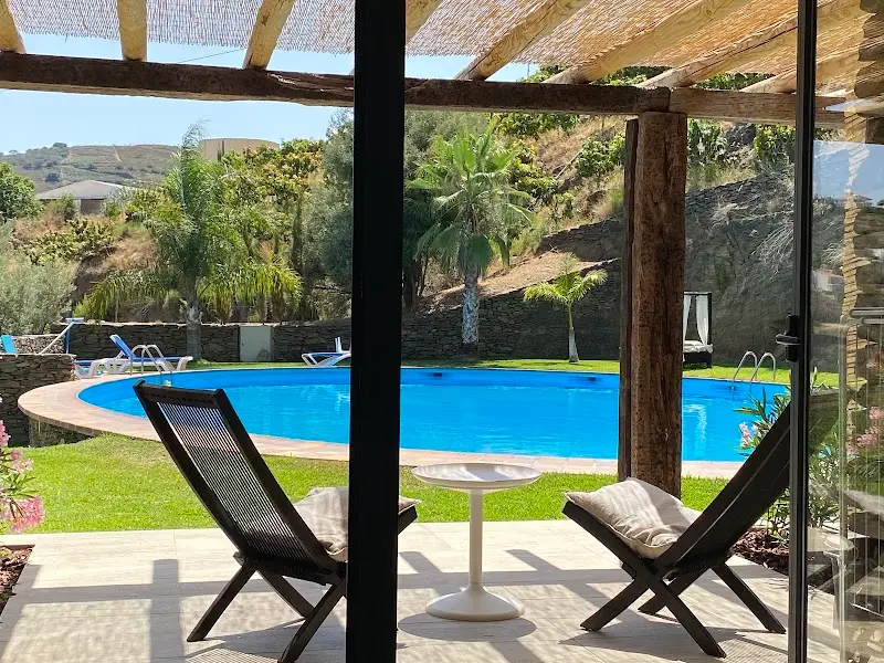 Porche con dos sillas de tijera y mesita frente a la piscina rodeada de jardín