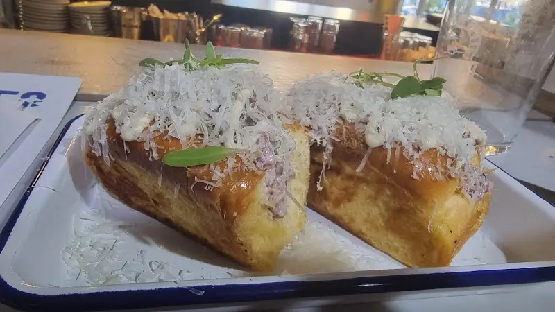 Dos bollos tostados rellenos y cubiertos de queso rallado y hojas de albahaca