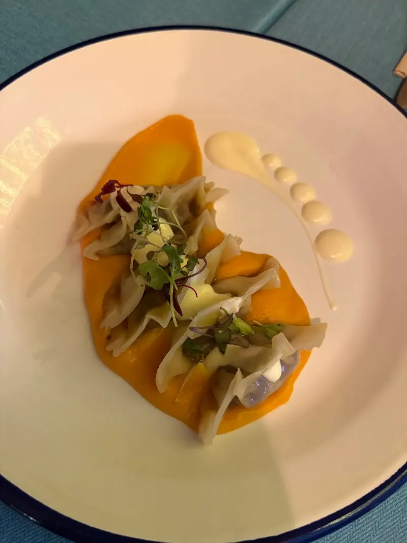 Pasta rellena sobre crema naranja con brotes verdes y puntos de salsa blanca