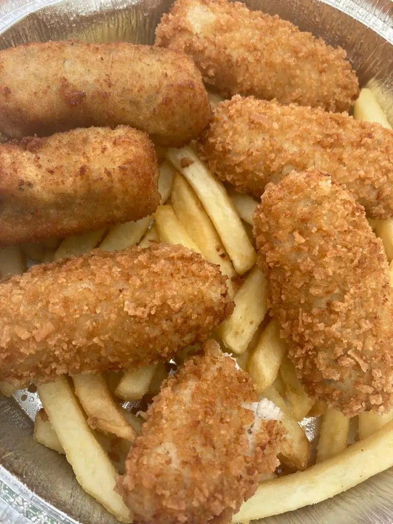Croquetas alargadas empanadas sobre patatas fritas en una bandeja de aluminio