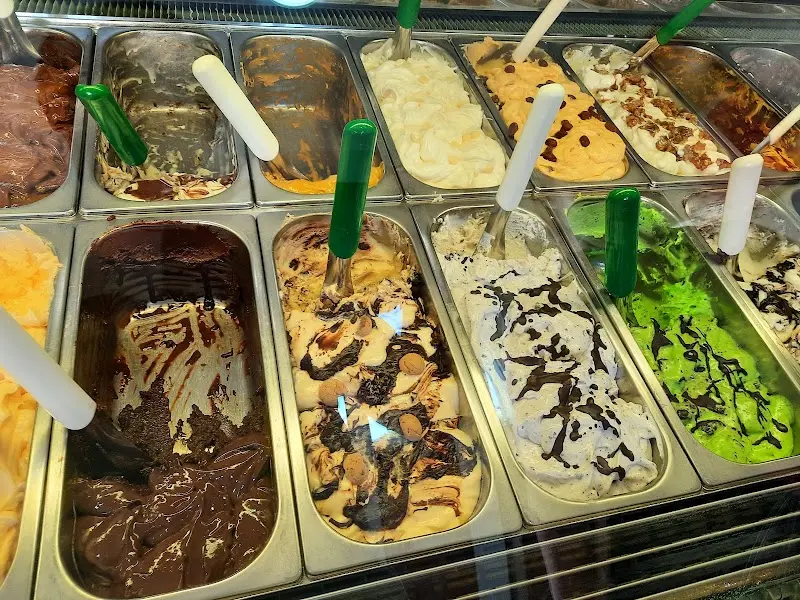 Helados de chocolate, pistacho, stracciatella y otros sabores con cucharas verdes en la vitrina