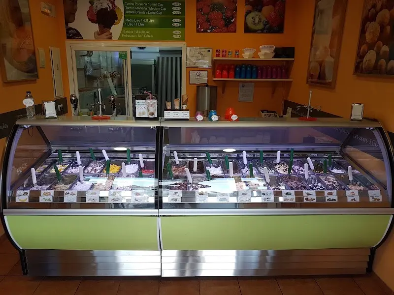 Vitrina curva de helados con decenas de sabores y lista de precios en la pared