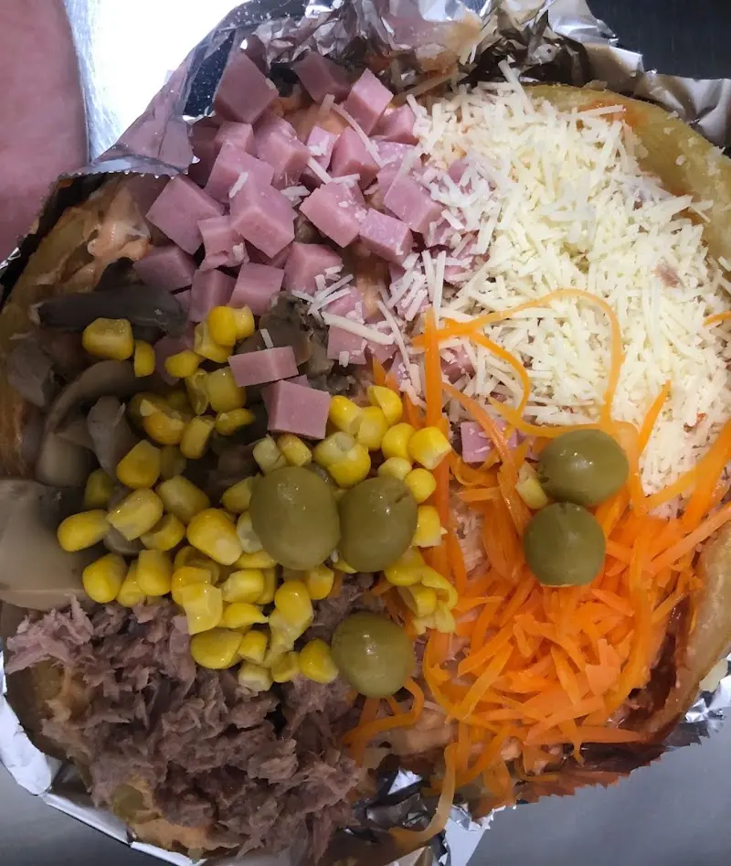 Patata rellena vista de cerca con atún, champiñones, maíz, jamón, queso rallado y aceitunas