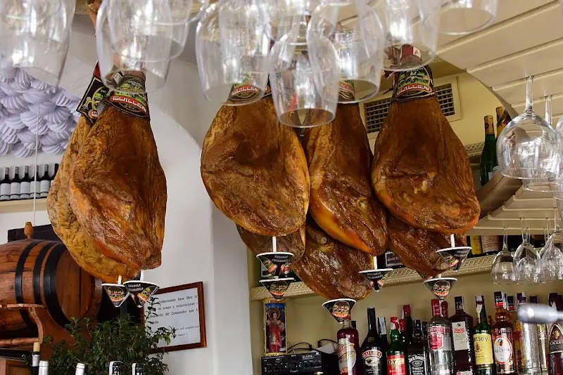 Jamones colgados sobre la barra junto a copas boca abajo y botellas de licor
