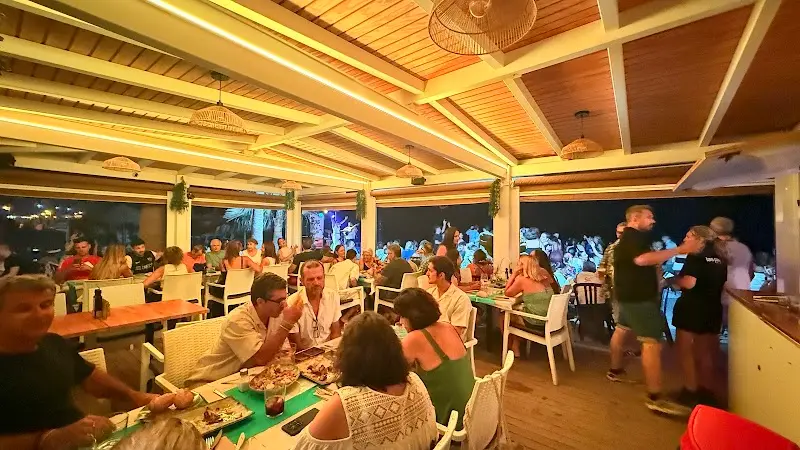 Comedor cubierto lleno de clientes cenando de noche, con techo de madera y lámparas