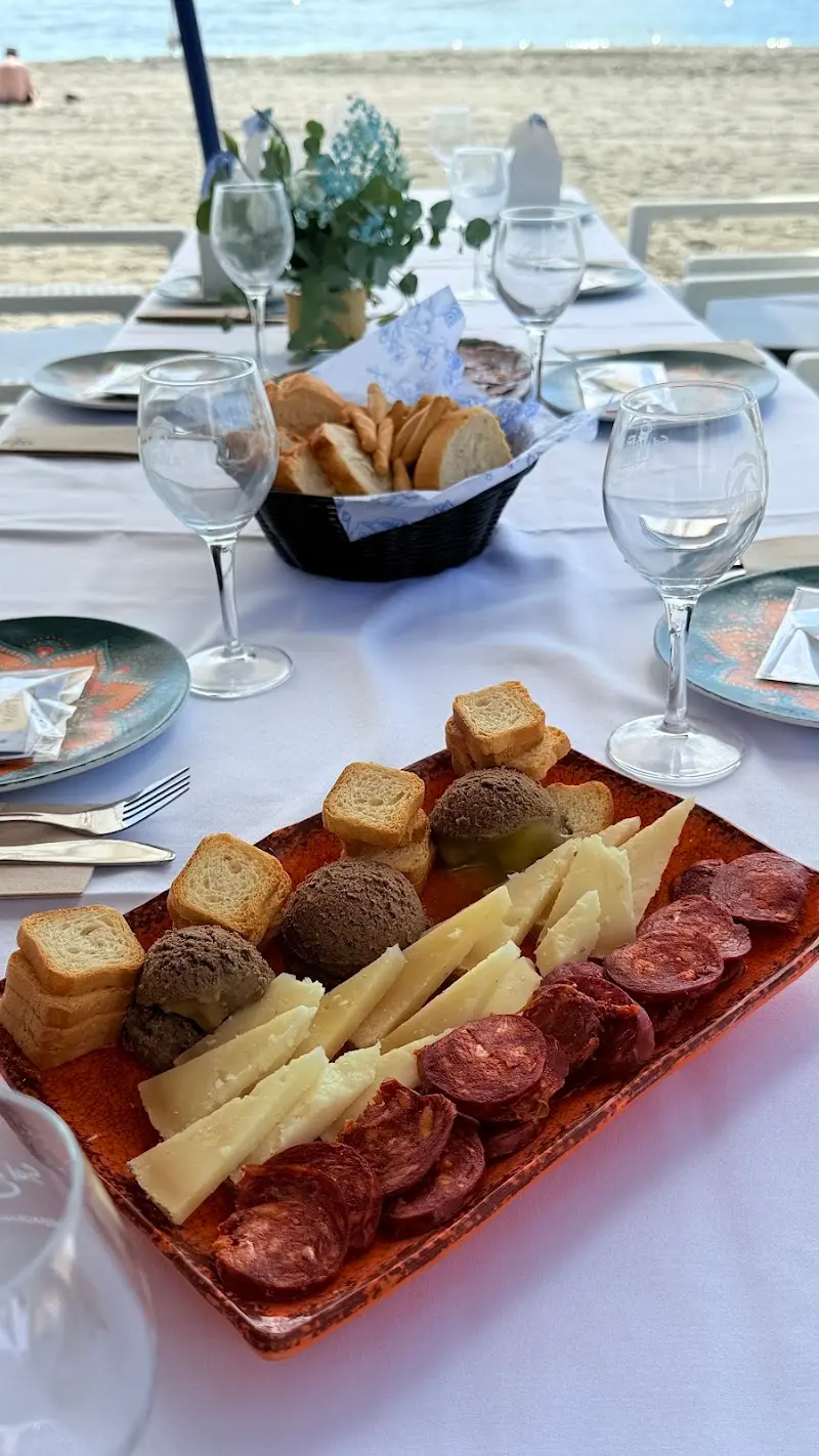 Tabla de queso, chorizo y paté con tostas en una mesa junto a la arena de El Playazo