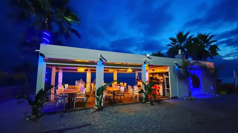Chiringuito iluminado con luces azules de noche, con mesas frente al mar