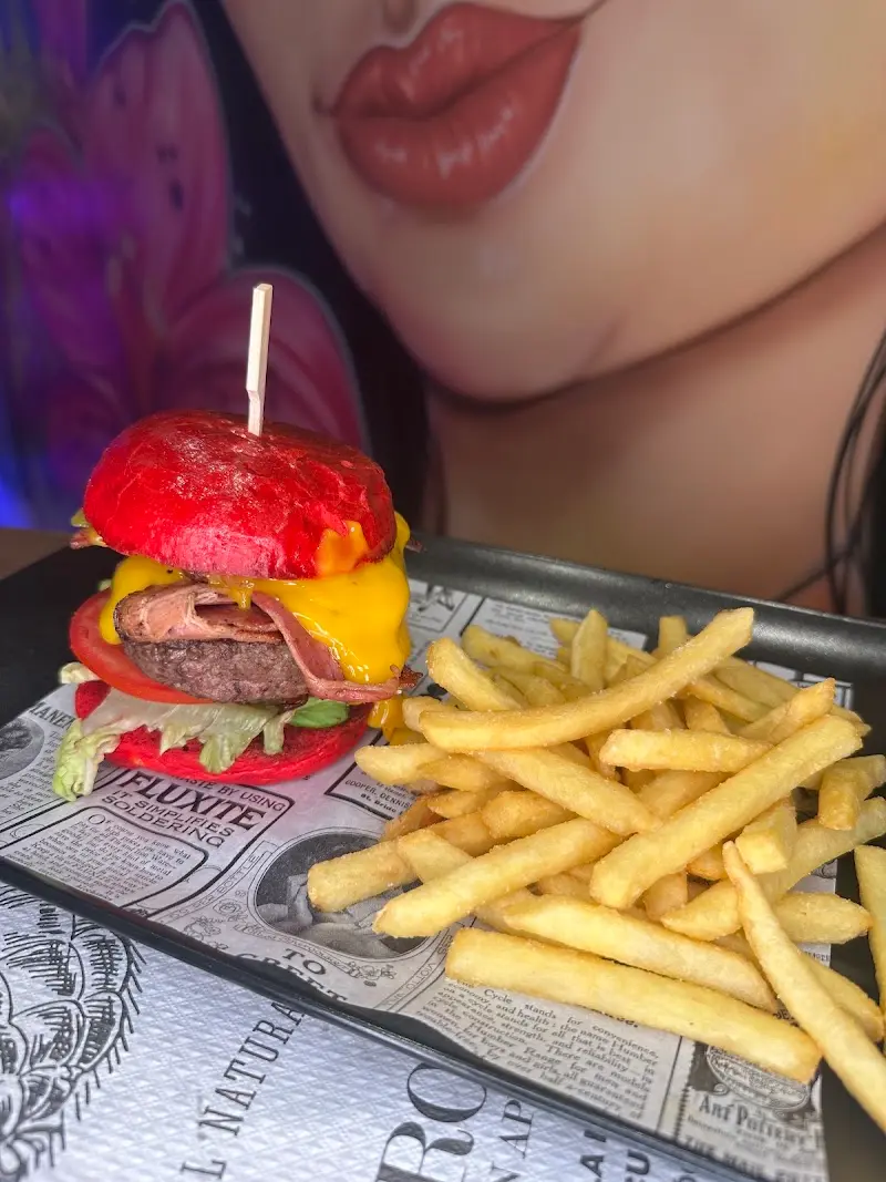 Hamburguesa con pan rojo, queso cheddar y beicon, con patatas fritas, ante un mural