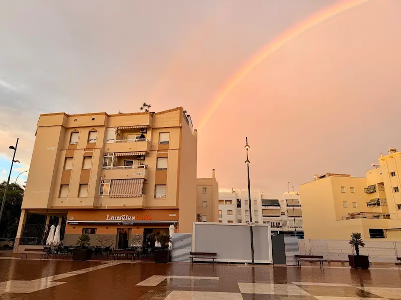 Edificio de Laureles Café en la plaza mojada tras la lluvia, con un arcoíris en el cielo