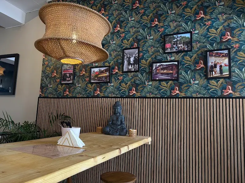 Rincón con papel pintado tropical, fotos enmarcadas, lámpara de mimbre y figura de Buda