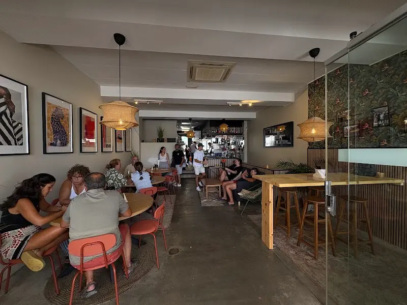 Comedor con mesas redondas, sillas naranjas, cuadros y lámparas de mimbre en Le Shack