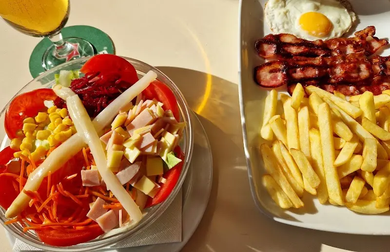 Ensalada mixta con espárragos y jamón york junto a un plato de beicon, huevo frito y patatas