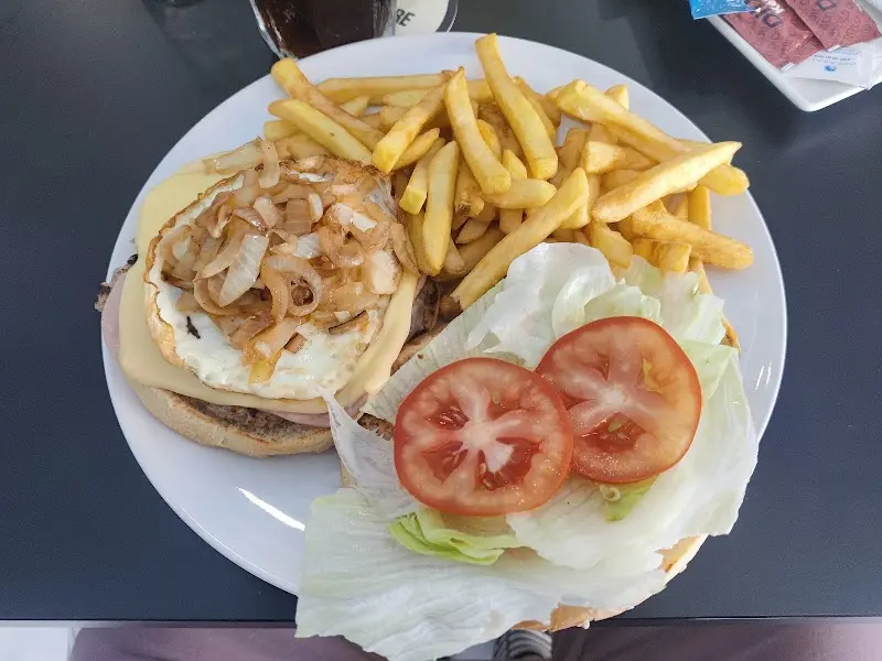 Hamburguesa abierta con huevo frito, queso y cebolla, con patatas fritas, lechuga y tomate