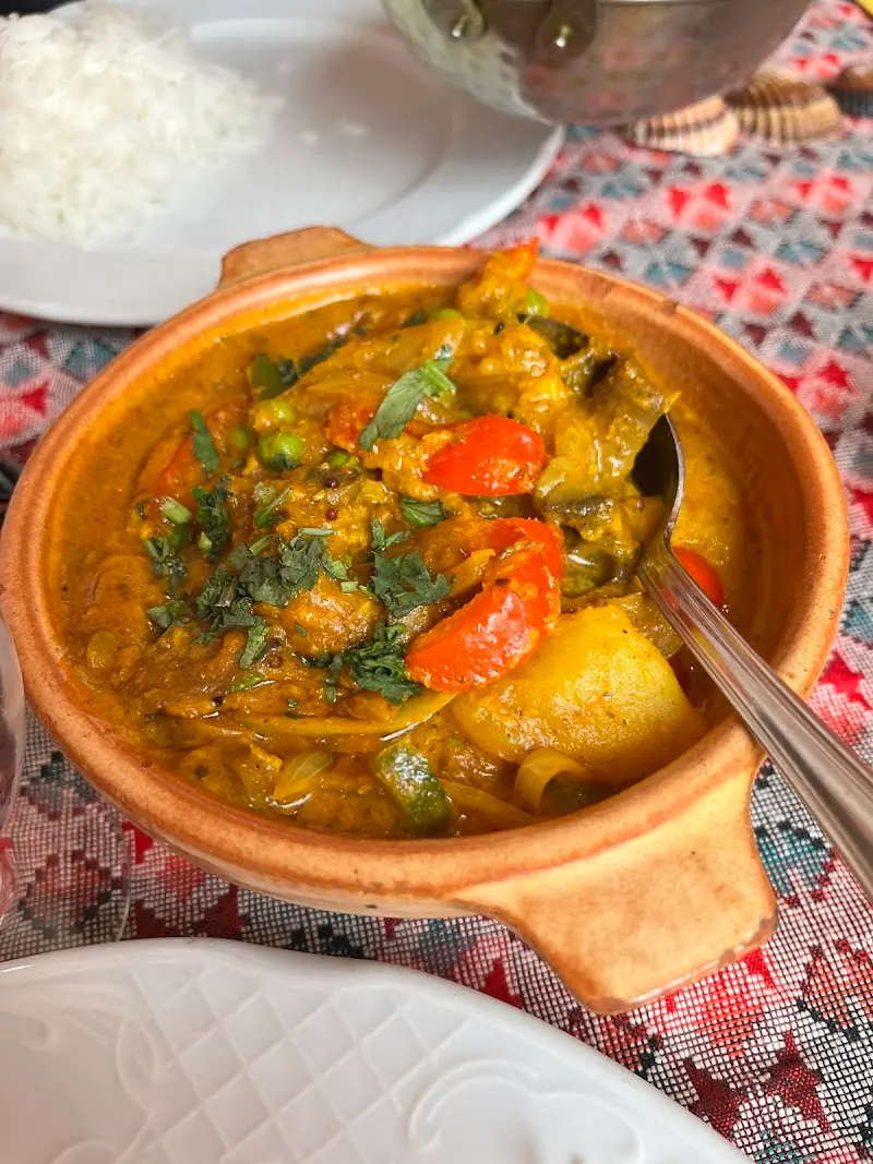Curry de verduras con patata, pimiento y guisantes en una cazuela de barro, con arroz