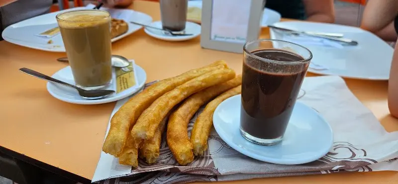 Churros con un vaso de chocolate caliente y un café con leche sobre la mesa