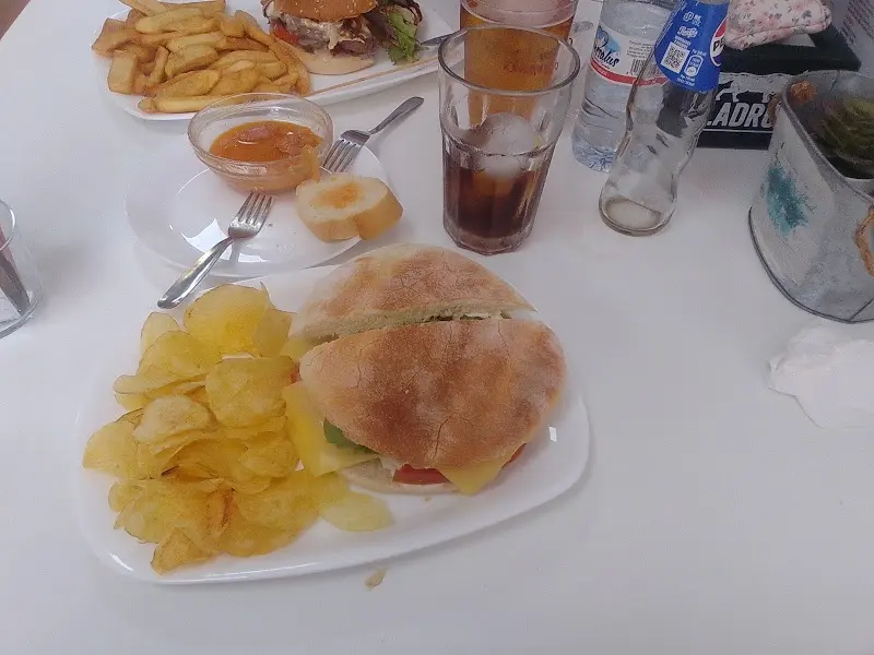 Sándwich de pan de chapata con patatas chips y refrescos en una mesa de Los Naranjos