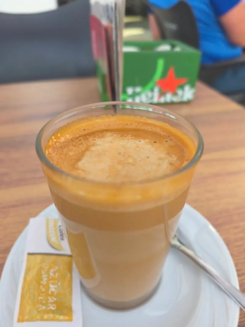 Café con leche en vaso de cristal con sobre de azúcar sobre una mesa de madera