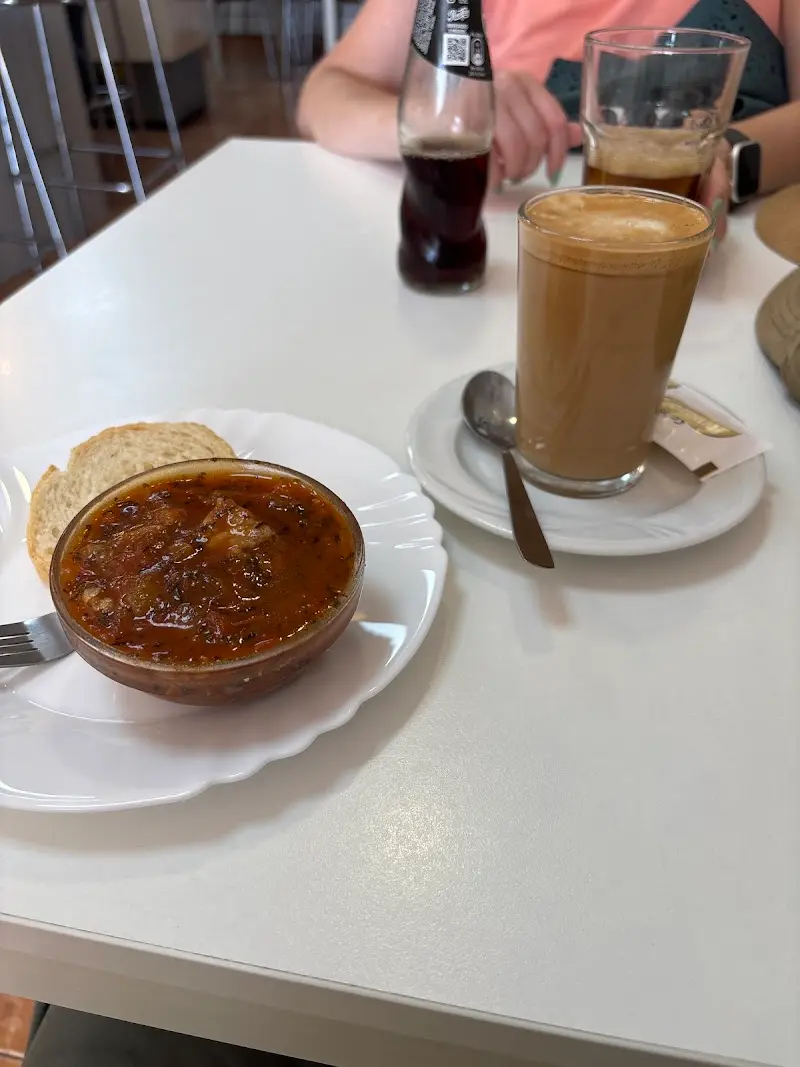 Cuenco de guiso con tomate y pan junto a un café con leche y un refresco