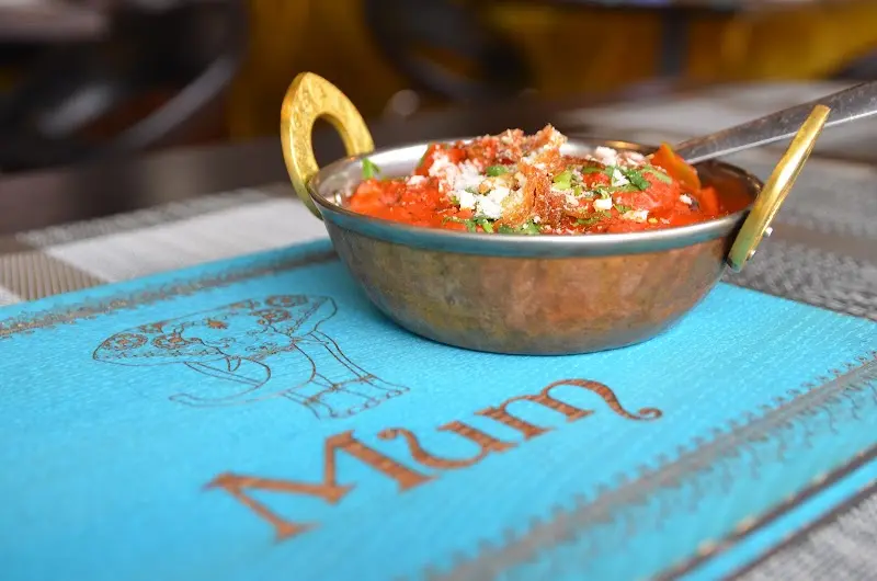 Curry rojo con queso desmenuzado en un cuenco de cobre sobre un mantel con el logo de Mum