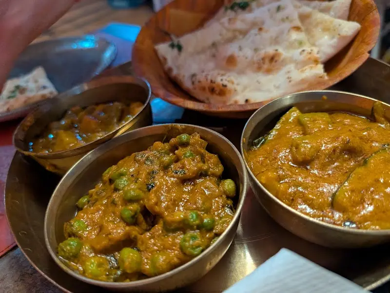 Cuencos de curry con guisantes y otros currys, junto a pan naan en un cesto de madera