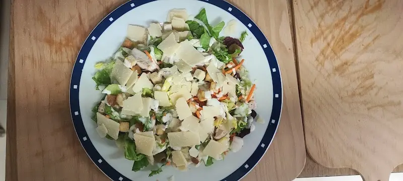 Ensalada verde con lascas de queso, picatostes y zanahoria en un plato de borde azul