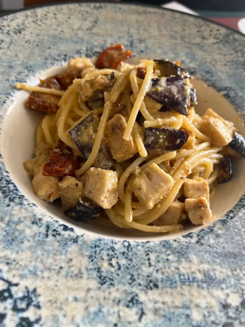 Espaguetis con dados de pollo, berenjena y tomate seco en un plato hondo