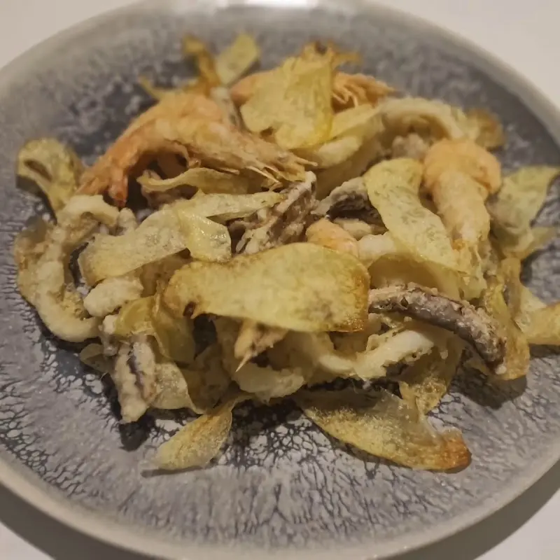 Fritura de gambas, calamares y láminas de patata crujiente en un plato gris