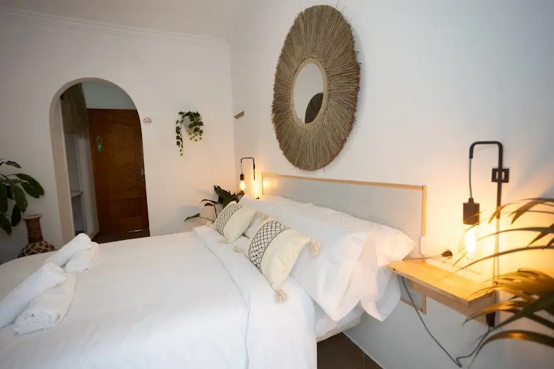 Dormitorio con cama de matrimonio blanca, espejo de fibra natural y puerta en arco