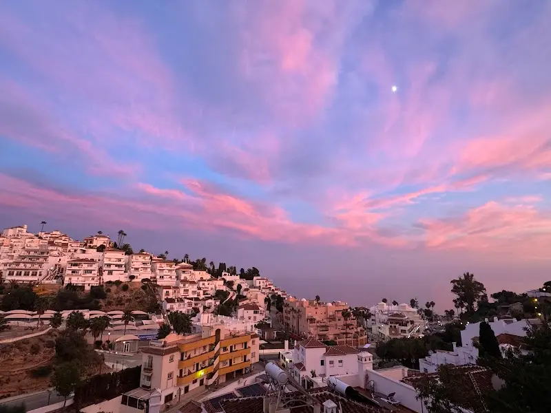 Atardecer con nubes rosas y la luna sobre las urbanizaciones blancas de la ladera